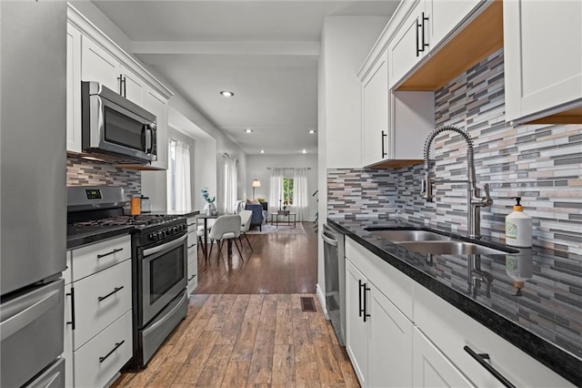 4421 Tracy Ave, Kansas City, MO 64110 - kitchen with stainless steel appliances, a sink, hardwood / wood-style floors, dark stone countertops, and white cabinetry