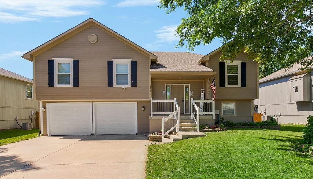 621 Muriel Dr, Grain Valley, MO 64029 - view of front of property featuring a garage, concrete driveway, a front yard, cooling unit, and a porch