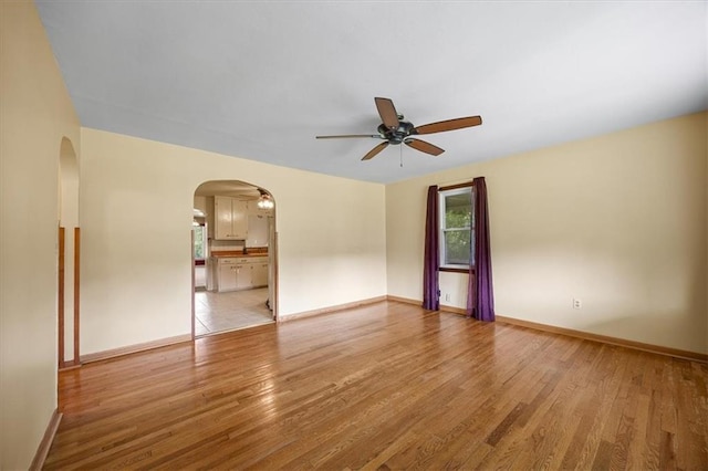 6608 N Edison Ave, Kansas City, MO 64151 - empty room featuring ceiling fan, light wood finished floors, arched walkways, and baseboards