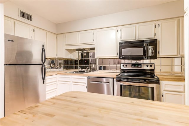 3606 Gillham Rd Unit 25, Kansas City, MO 64111 - kitchen with appliances with stainless steel finishes, a sink, tasteful backsplash, white cabinets, and butcher block counters