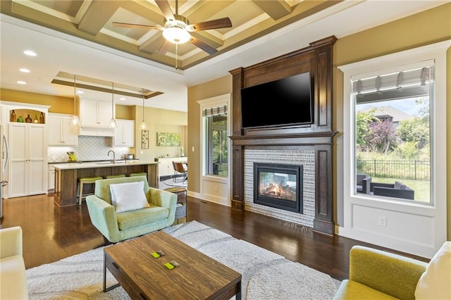 11446 S Longview Rd, Olathe, KS 66061 - living area featuring ceiling fan, a glass covered fireplace, dark wood-type flooring, ornamental molding, and coffered ceiling