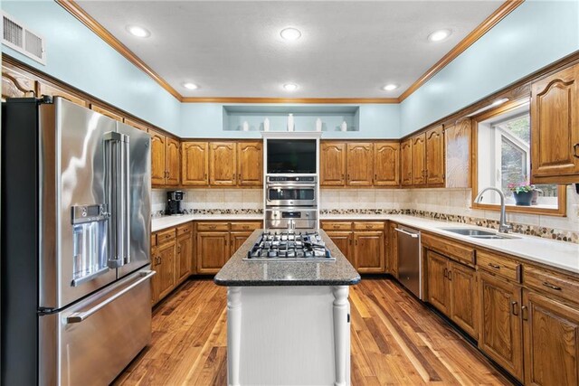 13008 Fontana St, Leawood, KS 66209 - kitchen with appliances with stainless steel finishes, a sink, brown cabinets, ornamental molding, and a center island