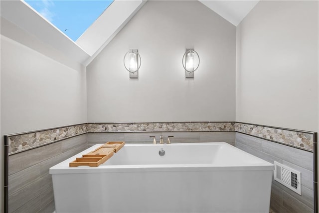 13008 Fontana St, Leawood, KS 66209 - full bathroom with tile walls, vaulted ceiling, a soaking tub, a wainscoted wall, and a skylight