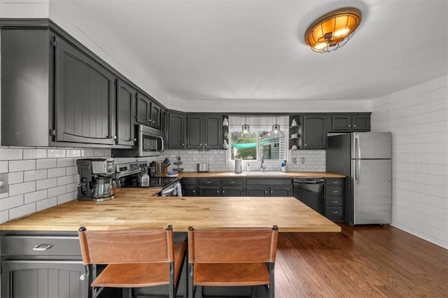 5741 Hadley St, Merriam, KS 66202 - kitchen with appliances with stainless steel finishes, wooden counters, dark wood-type flooring, a sink, and tasteful backsplash
