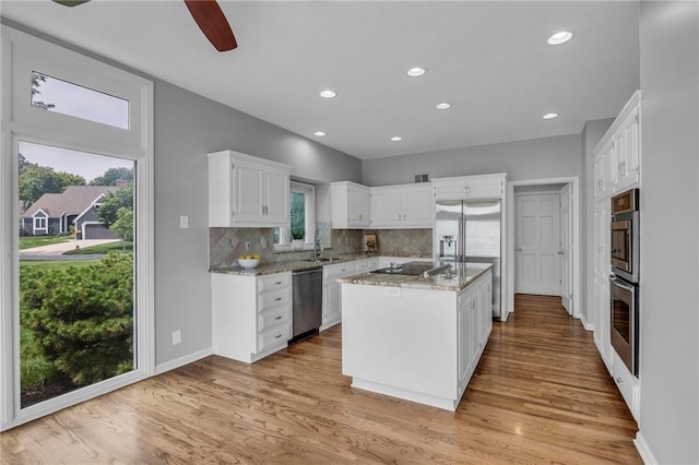 12428 Cambridge Cir, Leawood, KS 66209 - kitchen with appliances with stainless steel finishes, decorative backsplash, white cabinetry, a kitchen island, and light wood-style floors