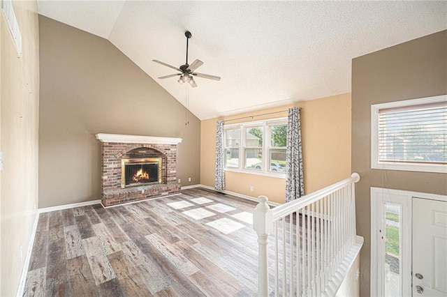 212 Hampton Dr, Smithville, MO 64089 - unfurnished living room featuring ceiling fan, high vaulted ceiling, wood finished floors, plenty of natural light, and a brick fireplace