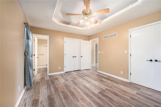 212 Hampton Dr, Smithville, MO 64089 - unfurnished bedroom featuring a textured ceiling, wood finished floors, a tray ceiling, ensuite bath, and a closet