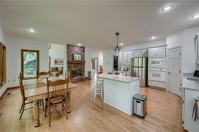 5317 NW Bluff Way, Parkville, MO 64152 - kitchen featuring white appliances, light wood finished floors, a fireplace, a center island with sink, and recessed lighting