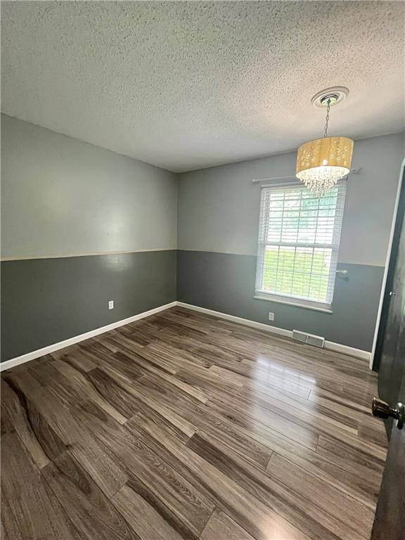 1 N Vine View St, Platte City, MO 64079 - empty room with wood finished floors, a textured ceiling, a chandelier, and baseboards