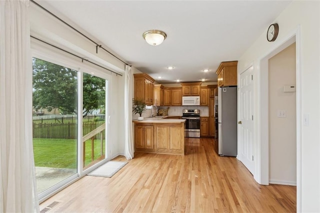 15050 W 145th St, Olathe, KS 66062 - kitchen featuring stainless steel appliances, a peninsula, light wood finished floors, decorative backsplash, and brown cabinets