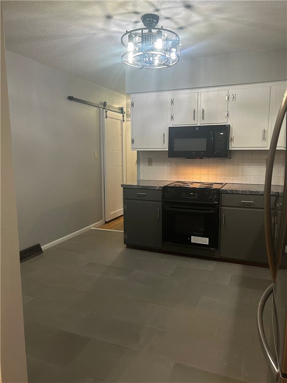 1923 Seneca St, Leavenworth, KS 66048 - kitchen with black appliances, a barn door, white cabinetry, decorative backsplash, and a textured ceiling