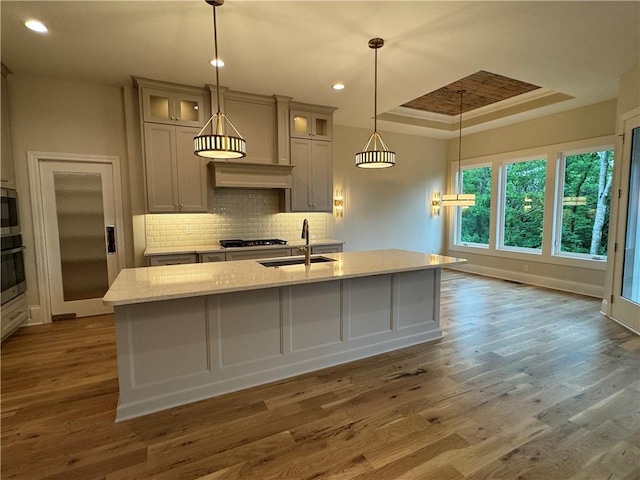 22428 W 90th Ter, Lenexa, KS 66227 - kitchen with a sink, a raised ceiling, a center island with sink, decorative backsplash, and wood finished floors