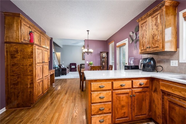 4422 N 122nd Ter, Kansas City, KS 66109 - kitchen featuring light wood-style flooring, a peninsula, a chandelier, brown cabinets, and light countertops