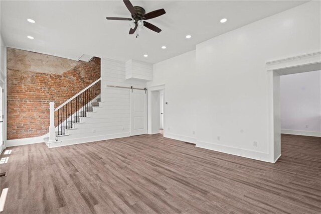 1003 Commercial St, Atchison, KS 66002 - unfurnished living room featuring a barn door, wood finished floors, brick wall, a ceiling fan, and baseboards