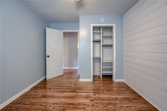 12800 W 100th St, Lenexa, KS 66215 - unfurnished bedroom featuring wood finished floors, a textured ceiling, a closet, wood walls, and baseboards