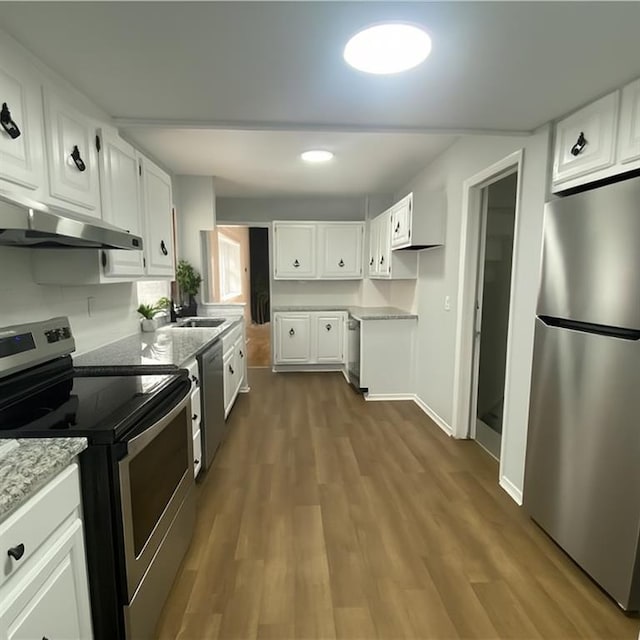3208 E 31st St, Kansas City, MO 64128 - kitchen with stainless steel appliances, under cabinet range hood, dark wood-type flooring, white cabinetry, and light stone countertops