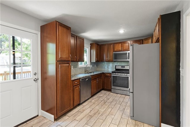 5317 NE 46th St, Kansas City, MO 64117 - kitchen with appliances with stainless steel finishes, a sink, light wood-style floors, backsplash, and dark stone counters