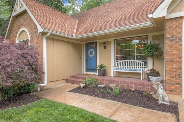 15243 Long St, Overland Park, KS 66221 - view of exterior entry featuring a shingled roof, a porch, brick siding, and stucco siding