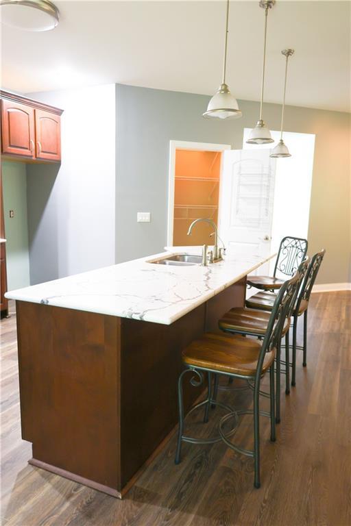 2404 Edmonds Ct, Columbia, MO 65203 - kitchen featuring a sink, dark wood-type flooring, a kitchen bar, hanging light fixtures, and light stone counters