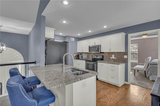 3708 N 112th St, Kansas City, KS 66109 - kitchen with appliances with stainless steel finishes, a sink, light wood-style flooring, a kitchen bar, and light stone countertops