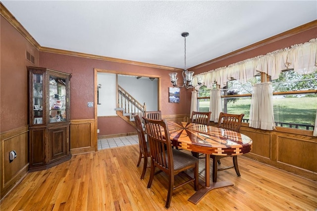 19819 Mclouth Rd, Tonganoxie, KS 66086 - dining area featuring a chandelier, light wood finished floors, crown molding, a wainscoted wall, and stairs