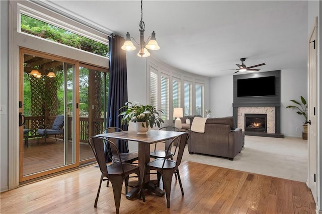 10154 N Lane Dr, Kansas City, MO 64157 - dining area featuring a warm lit fireplace, a ceiling fan, light wood-type flooring, and a chandelier