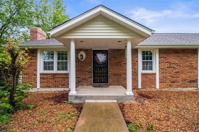 4188 Country Squire Ln, Oak Grove, MO 64075 - doorway to property featuring brick siding, a chimney, a shingled roof, and covered porch