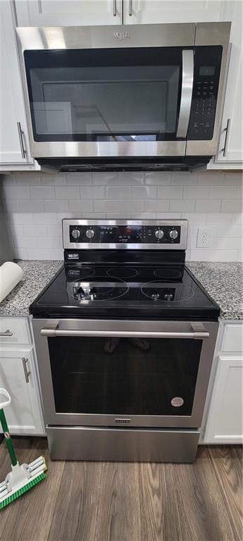 5118 Wabash Ave, Kansas City, MO 64130 - kitchen featuring appliances with stainless steel finishes, white cabinets, dark wood-style floors, light stone countertops, and decorative backsplash