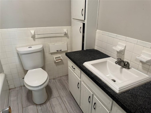 3006 S Santa Fe Rd, Independence, MO 64055 - bathroom featuring tile walls, toilet, vanity, wood finished floors, and a wainscoted wall