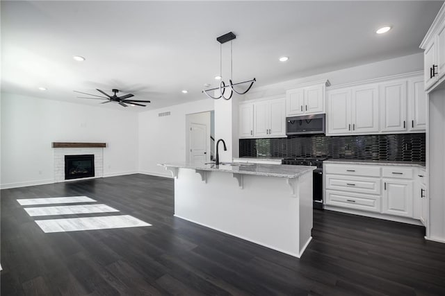 11147 Rowland Ave, Kansas City, KS 66109 - kitchen featuring stainless steel microwave, stove, a ceiling fan, decorative backsplash, and a breakfast bar area