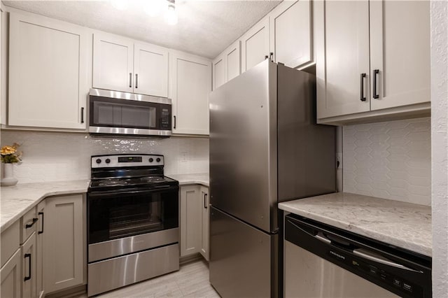 1617 N Pearl St, Independence, MO 64050 - kitchen featuring stainless steel appliances, backsplash, light stone counters, white cabinets, and a textured ceiling