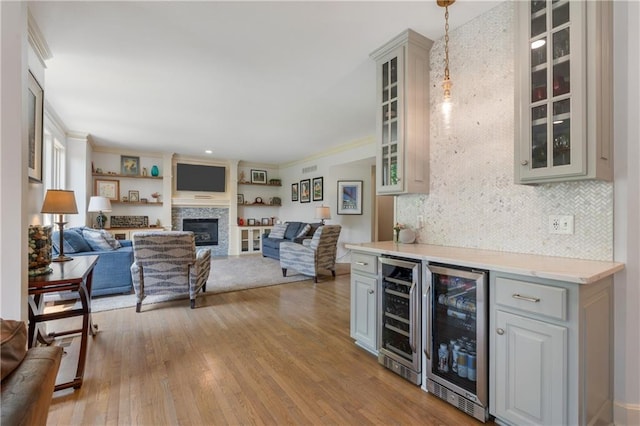13897 W 140th St, Olathe, KS 66062 - indoor dry bar featuring wine cooler, light wood finished floors, a glass covered fireplace, crown molding, and pendant lighting