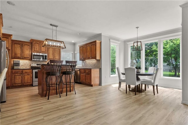 11412 S Lakecrest Dr, Olathe, KS 66061 - kitchen with stainless steel appliances, a chandelier, a breakfast bar area, brown cabinetry, and ornamental molding