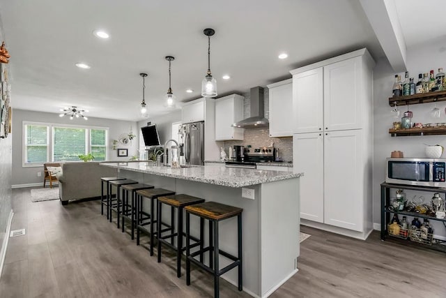 920 S Washington St, Independence, MO 64050 - kitchen with wall chimney range hood, appliances with stainless steel finishes, wood finished floors, white cabinetry, and a center island with sink