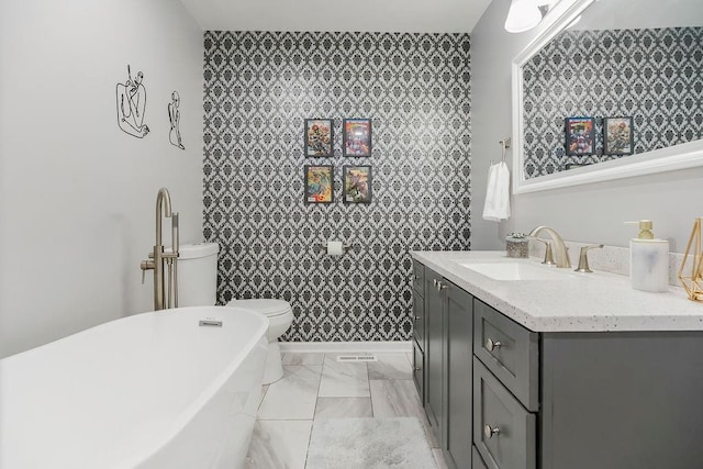 920 S Washington St, Independence, MO 64050 - bathroom featuring a freestanding bath, vanity, marble finish flooring, an accent wall, and toilet