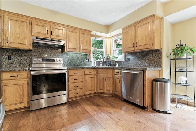 15206 W 85th St, Lenexa, KS 66219 - kitchen featuring stainless steel appliances, under cabinet range hood, light wood finished floors, dark countertops, and tasteful backsplash