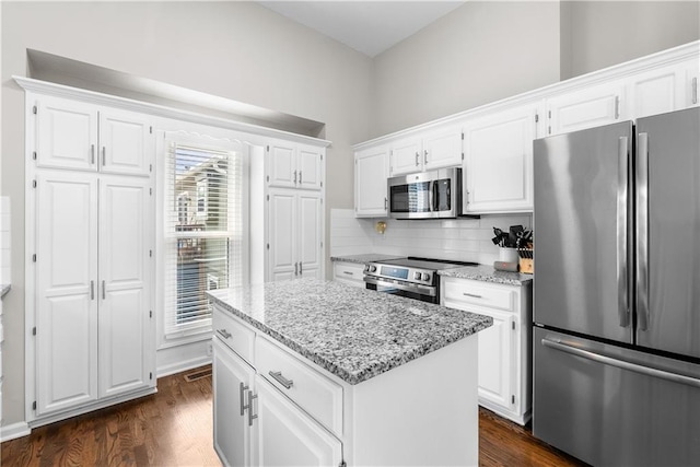 1021 NE Woodbury Ln, Lees Summit, MO 64086 - kitchen featuring appliances with stainless steel finishes, light stone counters, dark wood-style floors, white cabinetry, and a kitchen island