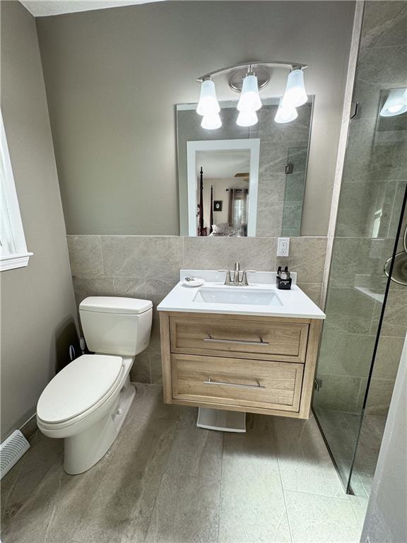 11500 Orchard Rd, Kansas City, MO 64134 - bathroom featuring tile walls, toilet, vanity, and a tile shower