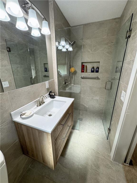 11500 Orchard Rd, Kansas City, MO 64134 - full bathroom featuring a stall shower, vanity, tile walls, and toilet