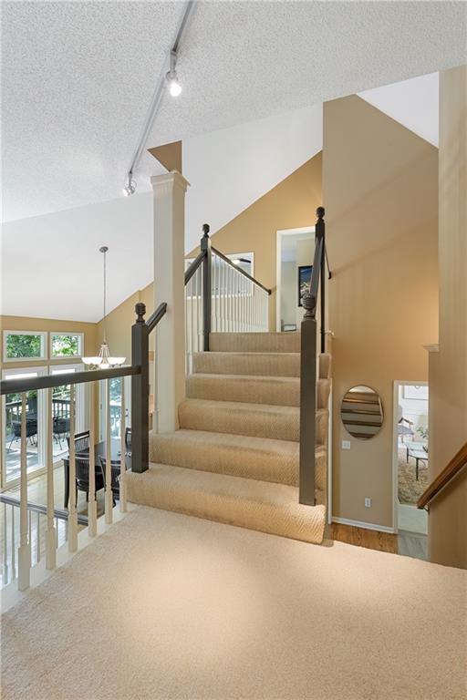 12577 S Alcan Cir, Olathe, KS 66062 - stairs with rail lighting, a textured ceiling, high vaulted ceiling, carpet, and a chandelier