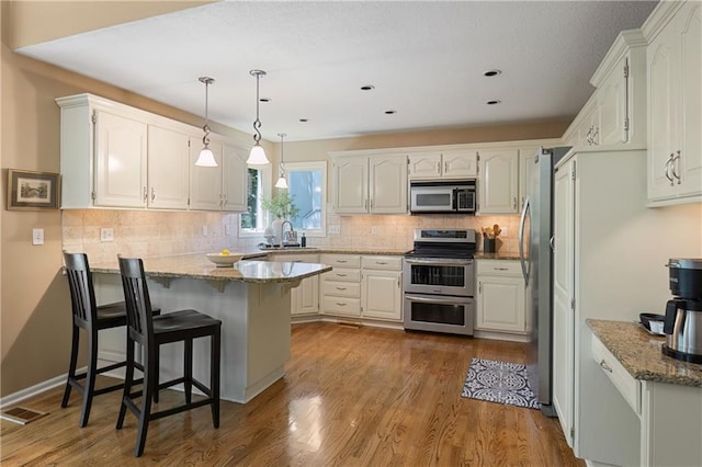 12577 S Alcan Cir, Olathe, KS 66062 - kitchen with stainless steel appliances, a peninsula, a breakfast bar, wood finished floors, and light stone countertops