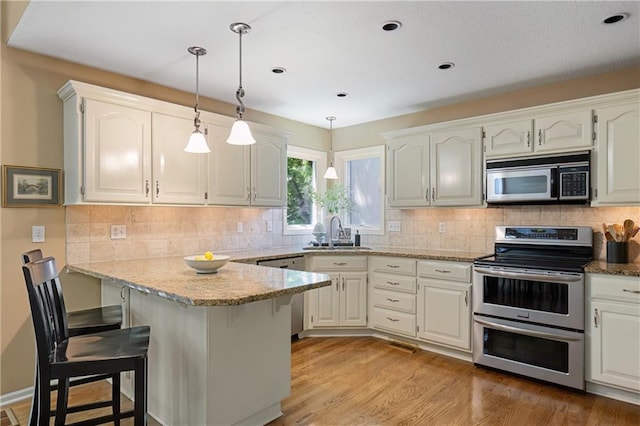 12577 S Alcan Cir, Olathe, KS 66062 - kitchen with appliances with stainless steel finishes, a peninsula, a kitchen breakfast bar, light stone countertops, and light wood finished floors