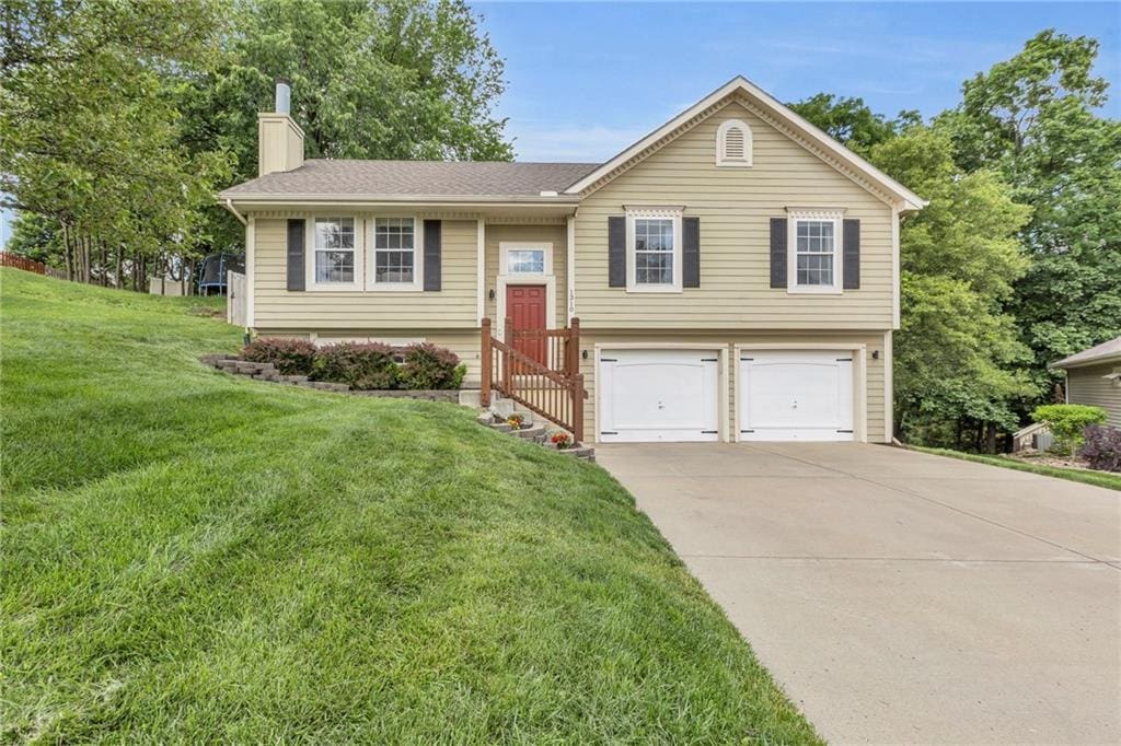 1310 NW 74th Pl, Kansas City, MO 64118 - raised ranch featuring an attached garage, a chimney, driveway, and a front lawn