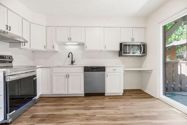 9599 Outlook Dr, Overland Park, KS 66207 - kitchen featuring appliances with stainless steel finishes, under cabinet range hood, white cabinetry, light countertops, and light wood finished floors