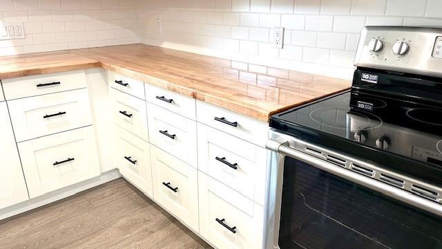 1636 S Poplar St, Ottawa, KS 66067 - kitchen featuring stainless steel range with electric stovetop, butcher block countertops, decorative backsplash, white cabinetry, and wood finished floors
