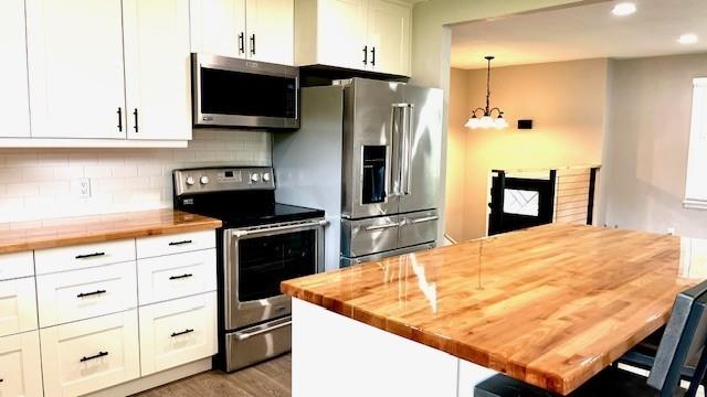 1636 S Poplar St, Ottawa, KS 66067 - kitchen with appliances with stainless steel finishes, butcher block countertops, a chandelier, white cabinets, and recessed lighting