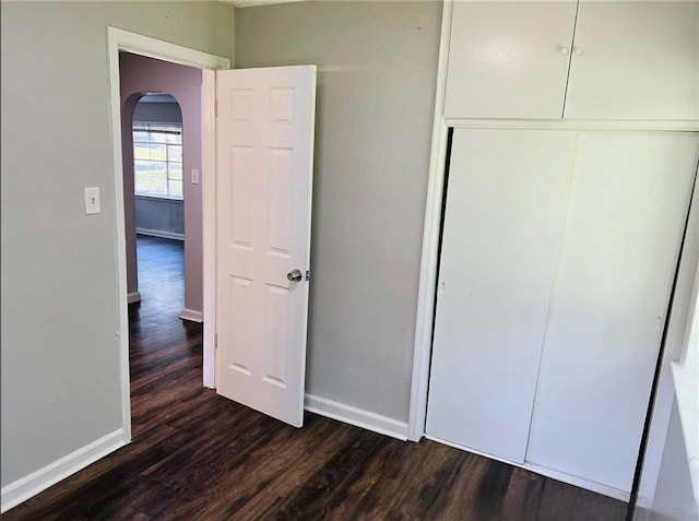 6823 S Benton Ave, Kansas City, MO 64132 - unfurnished bedroom with arched walkways, dark wood finished floors, baseboards, and a closet