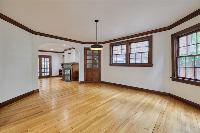 918 W 32nd Ter, Kansas City, MO 64111 - unfurnished living room featuring ornamental molding, arched walkways, plenty of natural light, light wood-style flooring, and baseboards