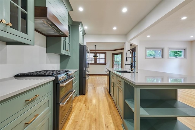 918 W 32nd Ter, Kansas City, MO 64111 - kitchen featuring green cabinetry, stainless steel appliances, a sink, wall chimney exhaust hood, and light wood-type flooring