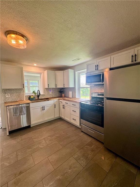 908 N 8th St, Lansing, KS 66043 - kitchen with appliances with stainless steel finishes, white cabinetry, plenty of natural light, decorative backsplash, and a textured ceiling